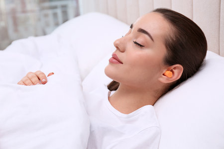 Young woman with foam ear plugs sleeping in bedの写真素材