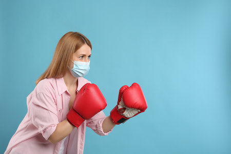 Woman with protective mask and boxing gloves on light blue background, space for text. Strong...