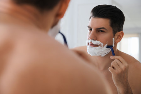 Handsome man shaving near mirror in bathroomの写真素材