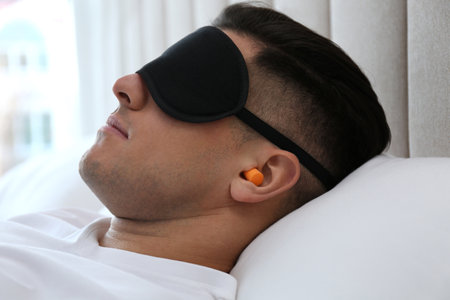 Man with foam ear plugs and mask sleeping in bed, closeupの写真素材