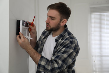 Man installing home security system on white wall in roomの写真素材