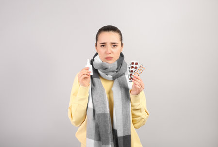 Woman with nasal spray and pills on light grey backgroundの写真素材