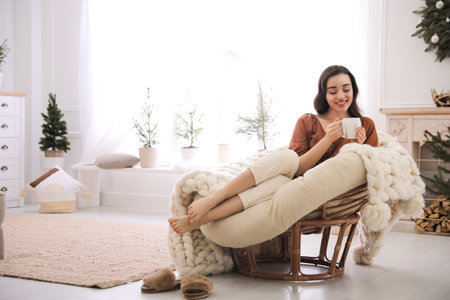 Woman with hot drink resting in comfortable papasan chair at home. Space for textの写真素材