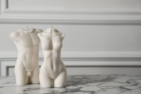 Stylish male and female body shaped candles on white marble table. Space for textの写真素材