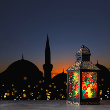 Decorative Arabic lantern on stone surface and silhouette of mosque at sunset on background, space for textの写真素材