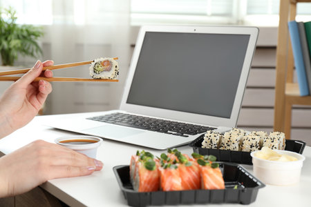 Woman having tasty sushi rolls for lunch at workplace, closeupの写真素材