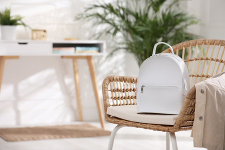 Stylish white backpack and jacket on wicker chair indoors, space for textの写真素材