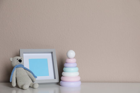 Empty photo frame, toy bear and ring pyramid on white table near gray wall. space for designの写真素材