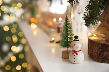 Funny ceramic snowman and small decorative tree on white table against blurred lights. Space for textの写真素材