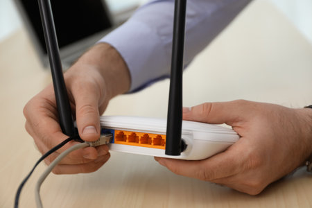 Man connecting cable to router at wooden table, closeup. wireless internet communicationの写真素材
