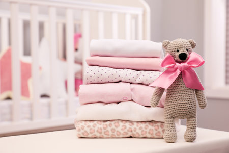 Stack of clean girl's clothes and toy bear on tableの写真素材