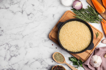 Flat lay composition with dry rice in wok on white marble table. Space for textの写真素材