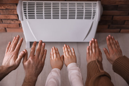 Family warming hands near electric heater at home, closeupの写真素材