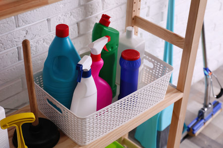 Plunger and basket with detergents on wooden shelf near white brick wall indoorsの写真素材