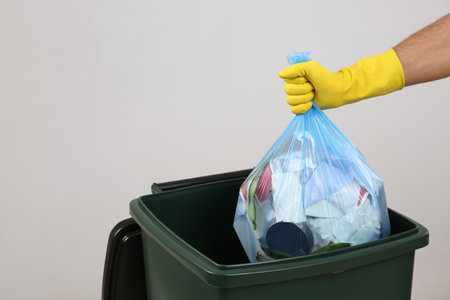 Man throwing garbage bag into bin on light background, closeup. Space for textの写真素材