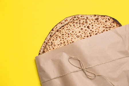 Tasty matzos wrapped with paper on yellow background, top view. Passover (Pesach) celebrationの写真素材