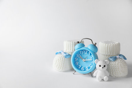 Alarm clock, toy bear and baby booties on white background, space for text. Time to give birthの写真素材