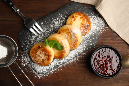 Delicious cottage cheese pancakes with icing sugar and jam on wooden table, flat layの写真素材