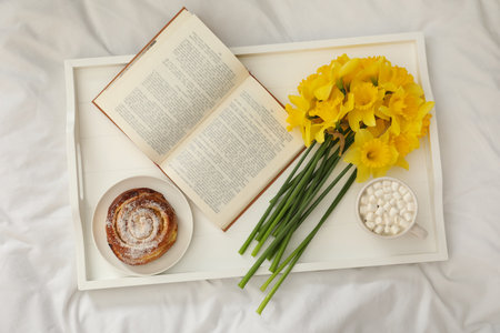 Bouquet of beautiful daffodils, bun and coffee on bed, top viewの写真素材