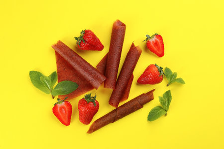 Delicious fruit leather rolls, mint and strawberries on yellow background, flat layの写真素材