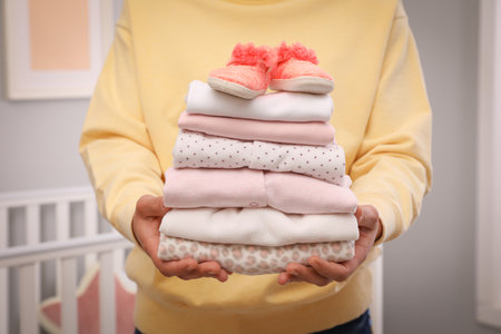 Woman holding stack of girl's clothes and booties indoors, closeupの写真素材