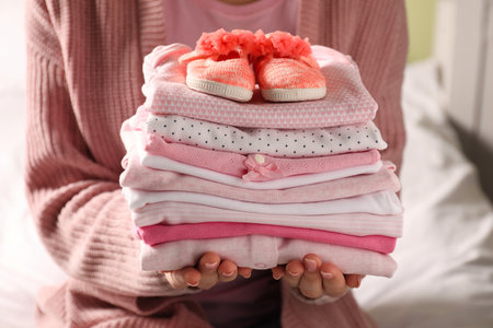 Woman holding stack of baby girl's clothes with shoes indoors, closeupの写真素材