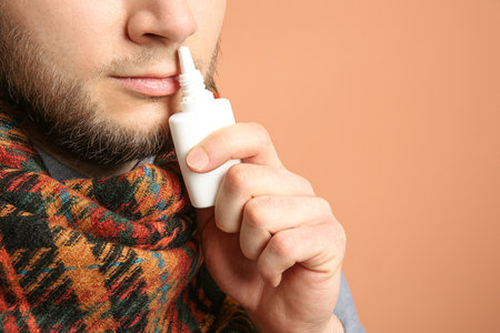 Sick man using nasal spray on orange background, closeupの写真素材