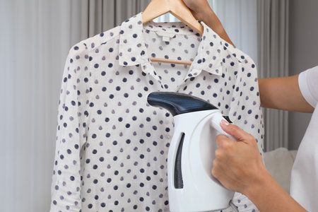 Woman steaming blouse on hanger at home, closeupの写真素材