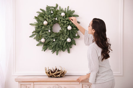 Young woman decorating Christmas wreath at homeの写真素材
