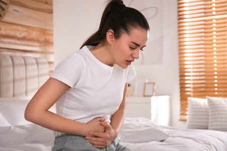 Young woman suffering from stomach ache on bed at home. food poisoningの写真素材