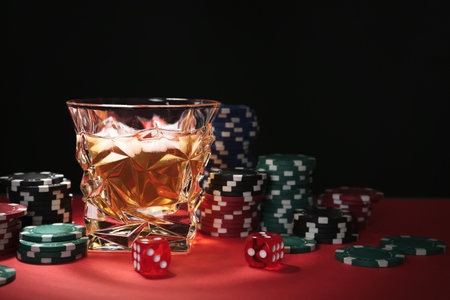 Casino chips, dice and glass of whiskey on red table against black background, space for textの写真素材