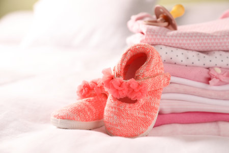 Stack of baby girl's clothes, pacifier and shoes on bed, closeup. Space for textの写真素材