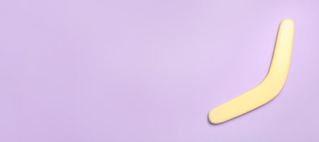 Yellow wooden boomerang on lilac background, top view. Space for textの写真素材