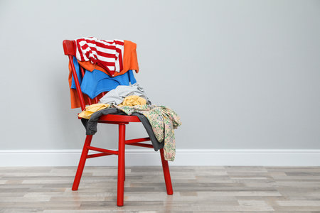 Different clothes on red chair near gray wall, space for textの写真素材