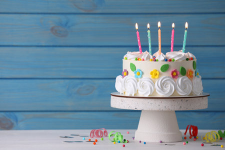 Delicious birthday cake and party decor on white wooden table against light blue background, space for textの写真素材