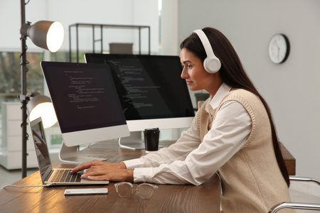 Programmer with headphones working at desk in officeの写真素材