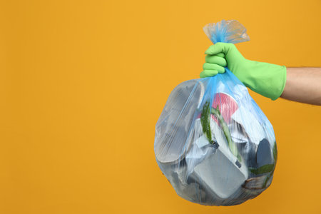 Man holding full garbage bag on yellow background, closeup. Space for textの写真素材
