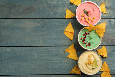 Different kinds of tasty hummus served with nachos on light blue wooden table, flat lay. Space for textの写真素材