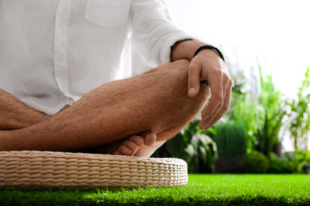 Young man meditating on straw cushion outdoors, closeupの写真素材