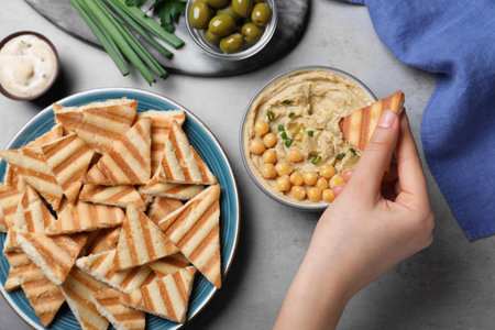 Woman dipping pita chip into hummus at gray table, top viewの写真素材