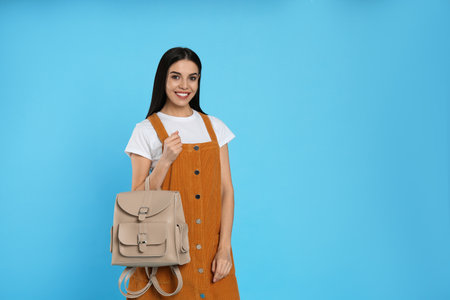 Young woman with stylish backpack on light blue background. Space for textの写真素材