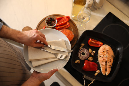 Tasty salmon steak and vegetables in frying pan, focus on plate with cutleryの写真素材