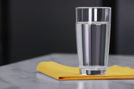 Glass of water and napkin on white table against blurred background. Space for textの写真素材