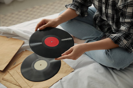Young woman choosing vinyl disc to play music with turntable on bed, closeupの写真素材