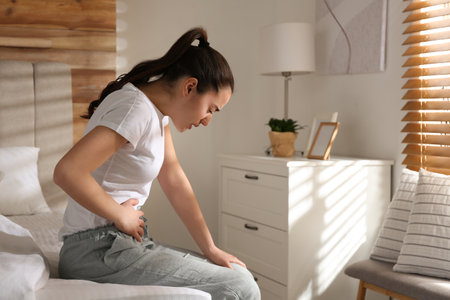 Young woman suffering from stomach ache on bed at home, space for text. food poisoningの写真素材