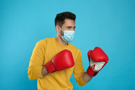 Man with protective mask and boxing gloves on light blue background. Strong immunity conceptの写真素材