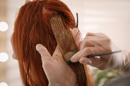 Professional hairdresser dyeing woman's hair with henna on blurred background, closeupの写真素材