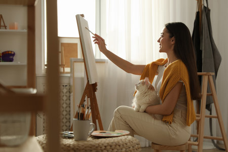 Beautiful young woman drawing on easel with cat at homeの写真素材