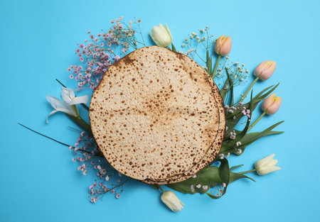 Tasty matzos and fresh flowers on light blue background, flat lay. Passover (Pesach) celebrationの写真素材