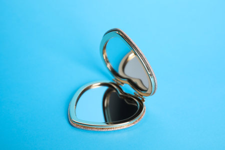 Stylish heart shaped cosmetic pocket mirror on light blue backgroundの写真素材
